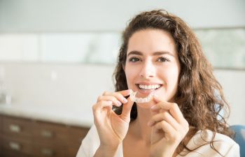 Woman with a perfect smile holding clear dental aligner.