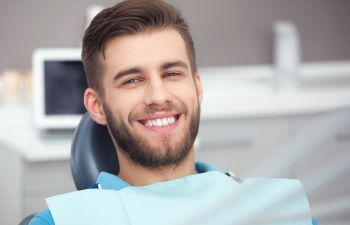 A young smiling man with perfect teeth sitting in a dental chair after fluoride treatment.