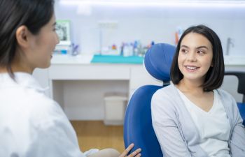 Dentist talking to a young woman sitting in a dental chair.