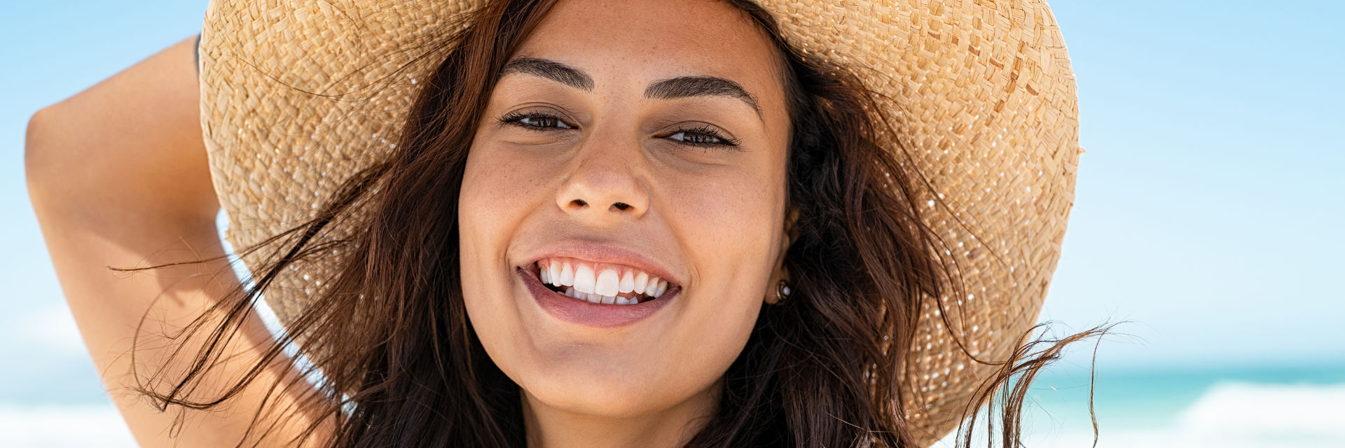 A beautiful young woman wearing a straw hat with a perfect smile.
