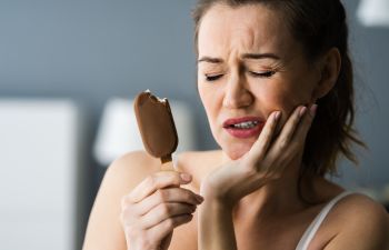 Woman suffering from teeth sensitivity pain caused by cold of ice-cream.