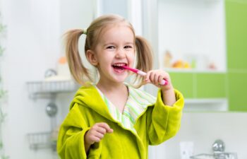 Smiling child kid girl brushing teeth in bathroom