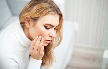 Pain. The problem of teeth. A woman feels pain in her tooth. A picture of a beautiful, sad girl suffering from severe pain in her teeth. An attractive woman feels painful toothache